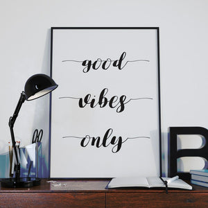 Good vibes only in black script above a desk with a black lamp